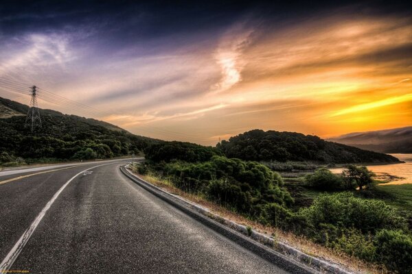 A estrada que se afasta ao pôr do sol entre a vegetação verde