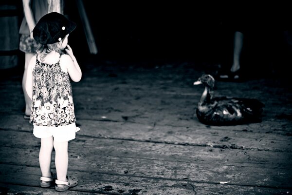 A girl in summer clothes in front of a woman on a black and white background watches a large black bird