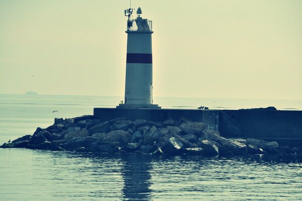 Ein Leuchtturm im Meer auf einem Betonsockel, der mit Steinen bedeckt ist