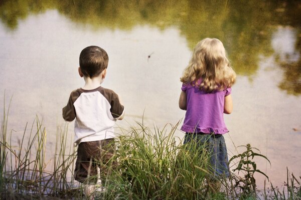 Children are standing on the shore of the pond