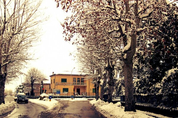 Foto von einer verschneiten Straße und einem gelben Gebäude hinter Bäumen