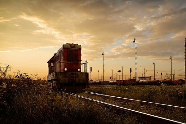 Le train de chemin de fer court le long de la voie ferrée, le ciel au-dessus de lui brille doucement, le bruit du coucher du soleil flotte dans le vent