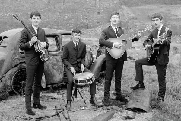 Beatles-Gruppe mit Musikinstrumenten vor dem Hintergrund eines alten, zerfallenen Autos