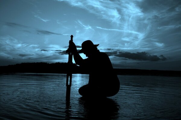 Silueta de un hombre con un sombrero contra el agua y el cielo