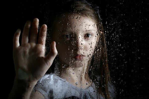 Fille regarde à travers le verre humide