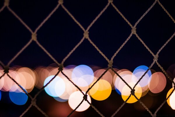 There are multicolored lights behind the fence net on a black background