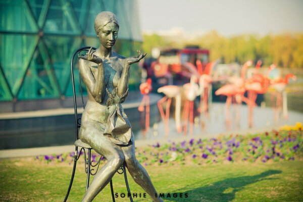 Statue of a girl sitting on a chair against a flamingo background