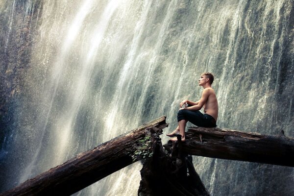 A man on a tree on the background of a waterfall