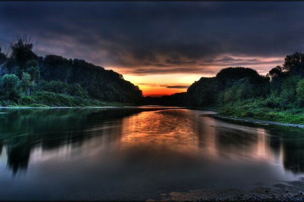 Ruhiger Fluss bei Sonnenuntergang unter dunklem Himmel