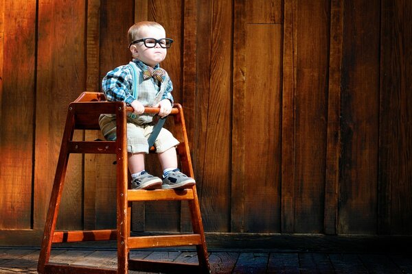 Un enfant à lunettes est assis sur une chaise en bois haut