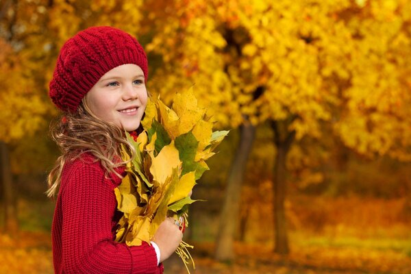 A girl in the autumn forest with an armful of yellow leaves