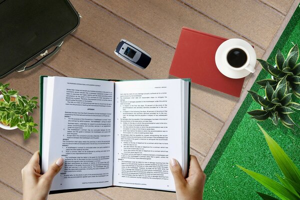 First-person photo of a girl reading a book on her desktop with a cup of coffee