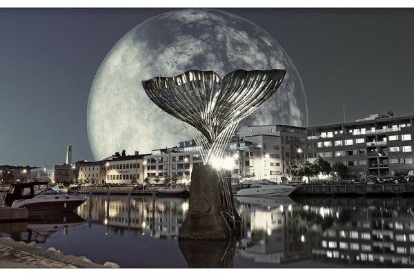 Un monumento en forma de cola de pez plateado sobresale del río contra el fondo de la Luna Poniente y la ciudad nocturna