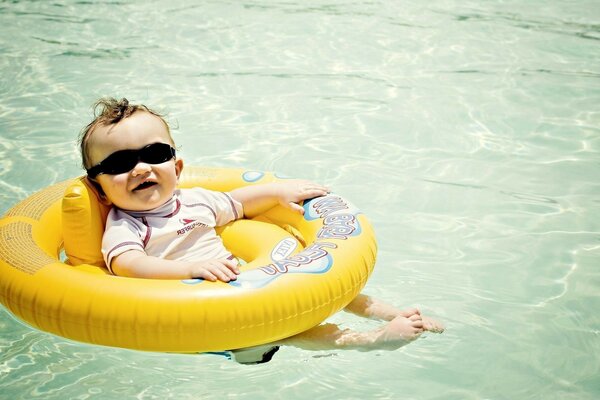 A child in sunglasses and a lifebuoy swims in the water