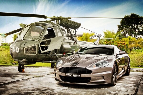 Ein Hubschrauber und ein Auto auf dem Parkplatz, dahinter Bäume und Gras