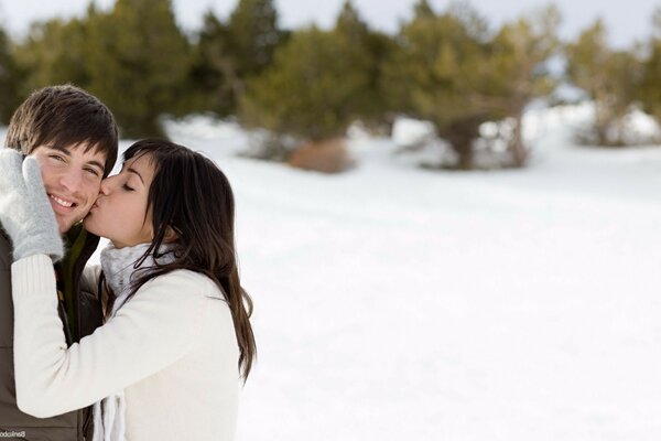 A girl kisses a guy in a snowy clearing