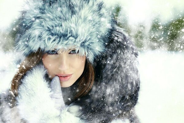 Una ragazza con un cappello soffice è spruzzata di neve