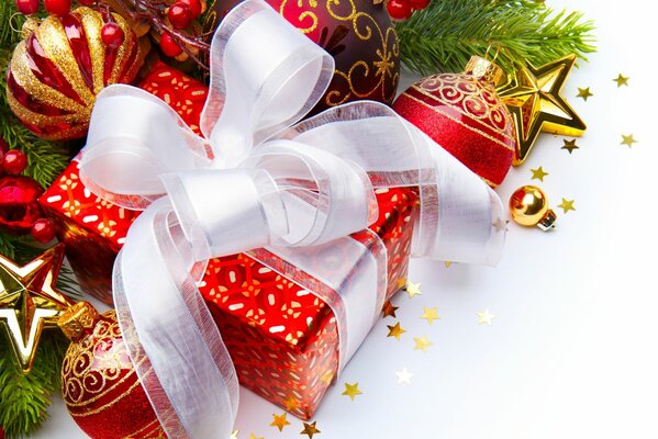 क्रिसमस के खिलौने और देवदार की शाखाओं के बीच एक सफेद धनुष के साथ एक लाल उपहार बॉक्स