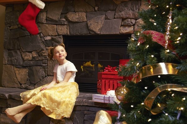 Esperando un milagro. Una niña junto a la chimenea y un árbol de Navidad vestido. Serpentina