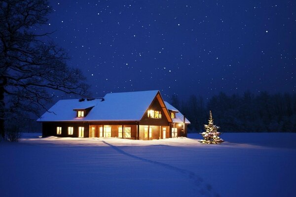 Casa en la noche en la nieve con un árbol de Navidad
