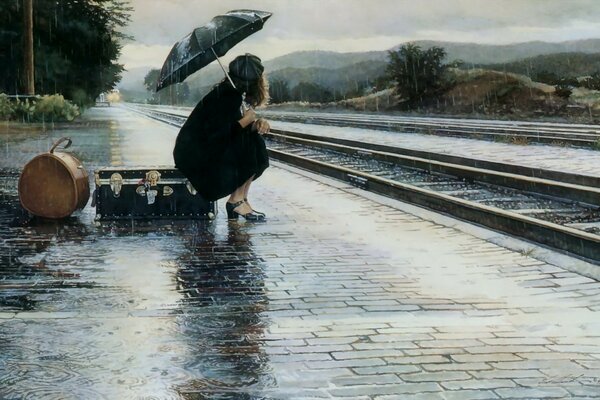 The girl is sitting under an umbrella near the railway