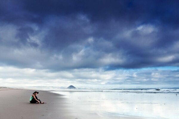 A girl is sitting on the seashore with dark clouds in the sky