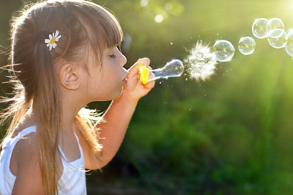 A girl with a daisy in her hair blows soap bubbles