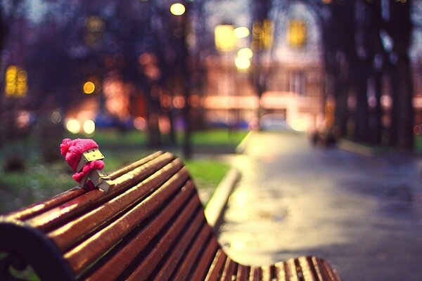 A wooden man, dressed in autumn, sits on the back of a bench