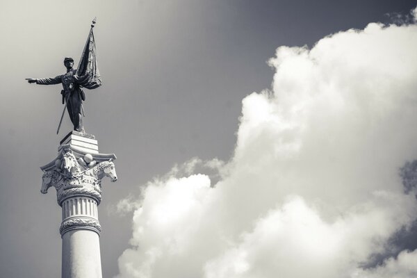 Escultura sobre un pedestal con una bandera contra el cielo