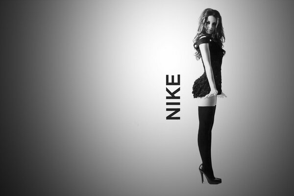 A girl in high heels in a mini next to the Nike inscription in black and white