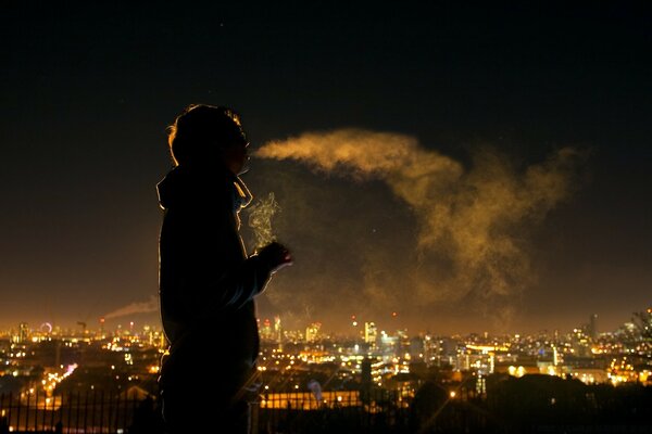 A man smokes against the background of the evening city