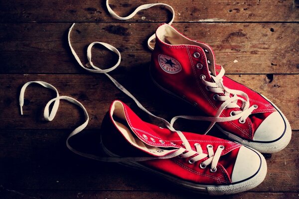 Coppia di scarpe da ginnastica rosse Converse sul pavimento di legno con lacci delle scarpe sparsi