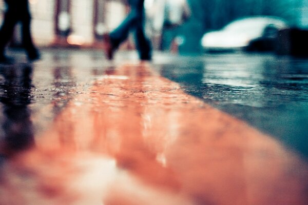 Macro di una strada asfaltata bagnata dalla pioggia percorsa dalle persone