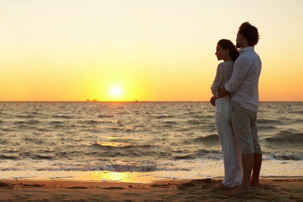 Pareja enamorada en la orilla del mar en medio de la puesta de sol