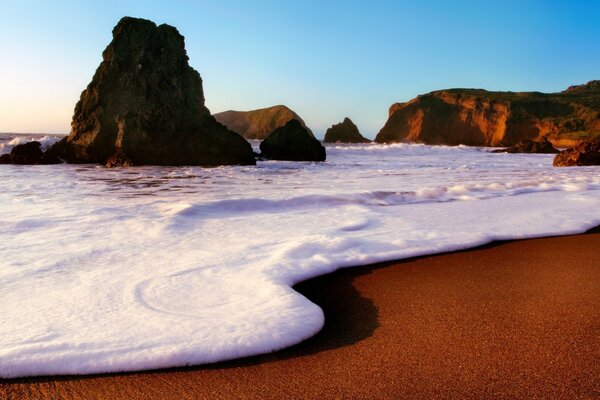 Onde schiumose rotola su una spiaggia di sabbia