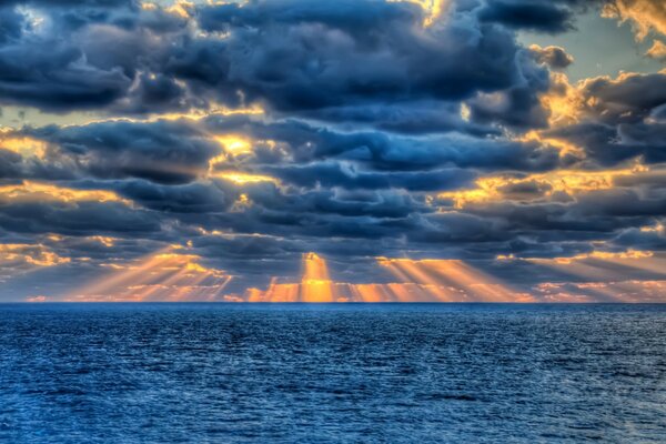 Güneşin ışınları denizin arka planına karşı bulutların arasından geçiyor