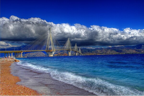 Le pont sur la mer va dans les nuages. Ciel bleu. Sable jaune