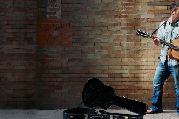 一个街头音乐家为路人弹吉他，站在砖墙上