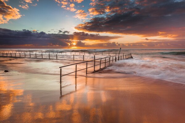 Sea waves break on the railing dug in on the beach