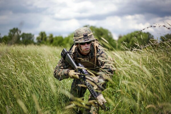 A uniformed soldier makes his way through the tall grass in a field