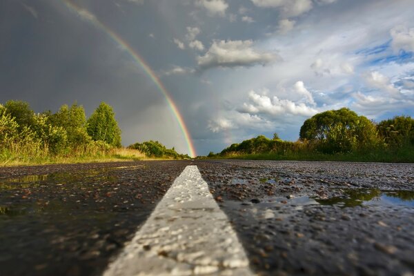 Die Straße, die in einen Regenbogen und einen bewölkten Himmel übergeht