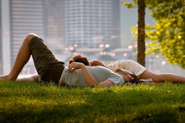 A couple in love is lying on the grass in a big city park