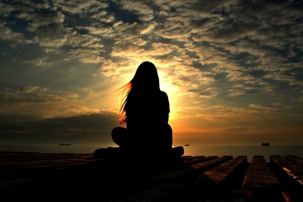 Silhouette d une jeune fille assise dans une pose de Lotus fermé par le soleil