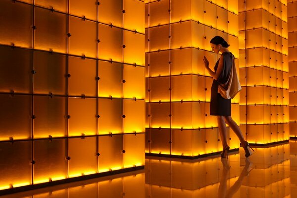 The girl stands at the illuminated architectural wall