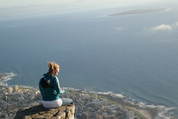 A brave girl is sitting on the edge of a cliff above the city