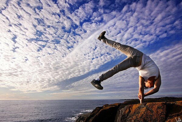 The kid performs a one-handed stand on the edge of a cliff