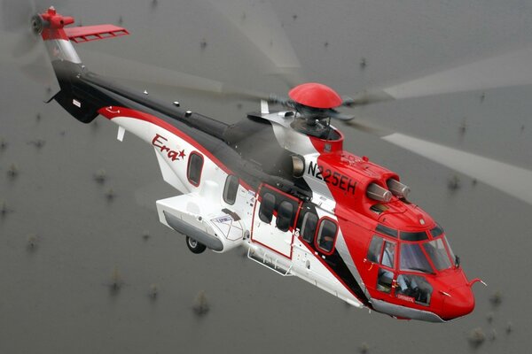 A red helicopter flies over the surface of the ocean