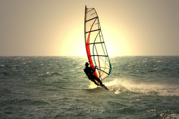 A man under sail rushes through the waves to meet the sun