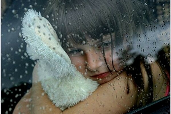 Criança com brinquedo olha pela janela com gotas de chuva