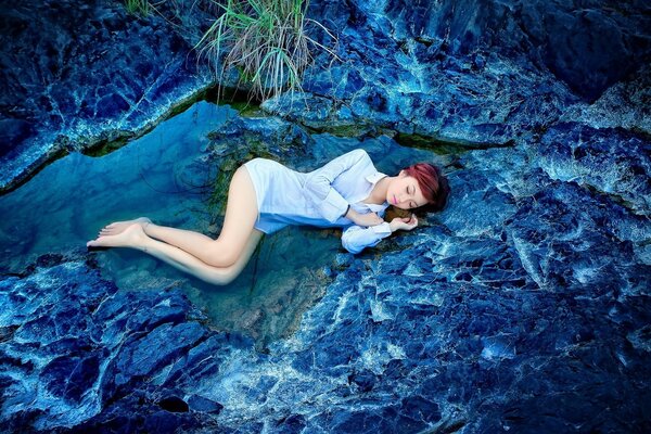 A girl in a white shirt is lying on her side in the water. Landscape in blue colors